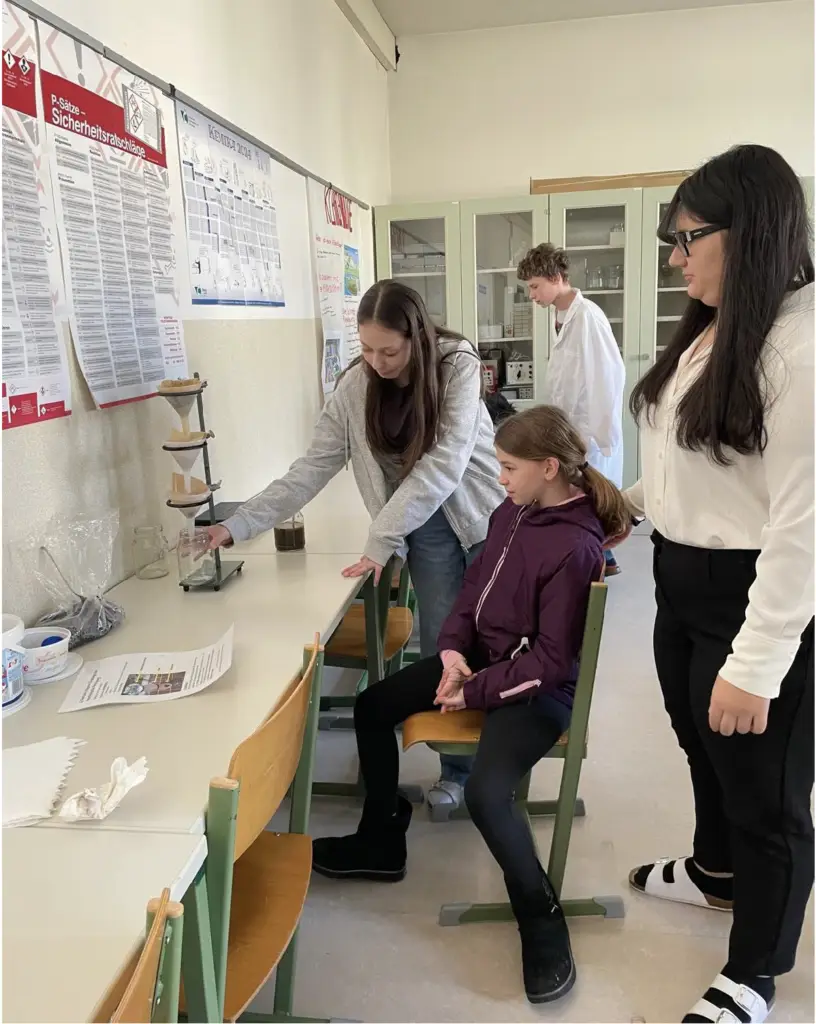 Sch&uuml;lerinnen f&uuml;hren im Chemieraum ein Wasserfilter-Experiment mit Trichter durch.
