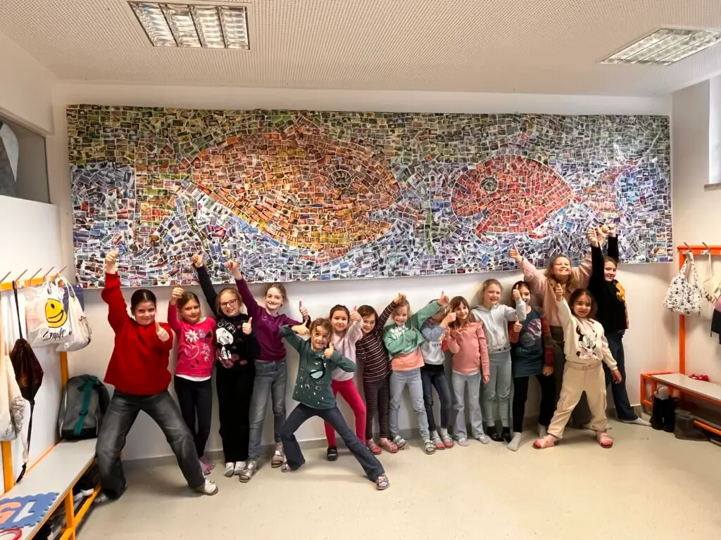 Schulklasse posiert vor gro&szlig;em Fisch-Mosaik aus Fotos im Gang.